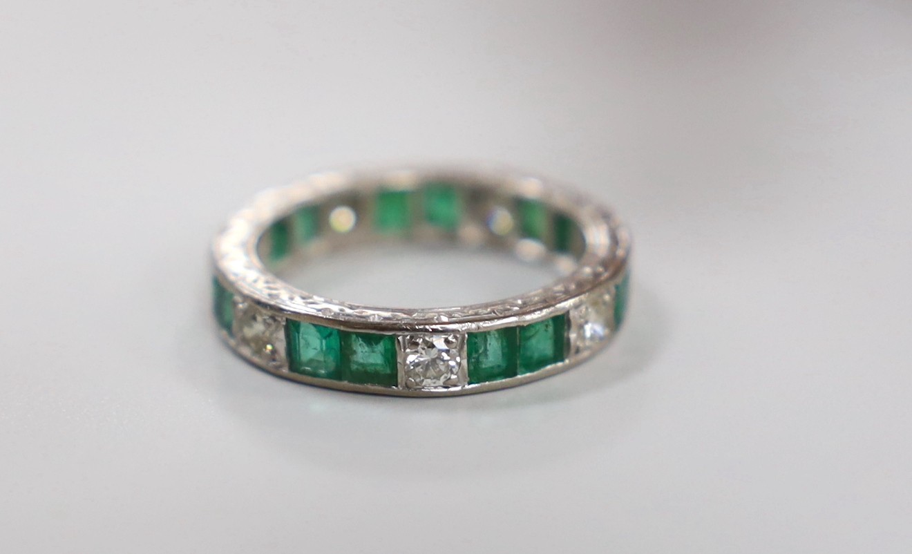 A mid 20th century 18ct white metal, emerald and diamond set full eternity ring (a.f.), size M/N, gross weight4.9 grams.